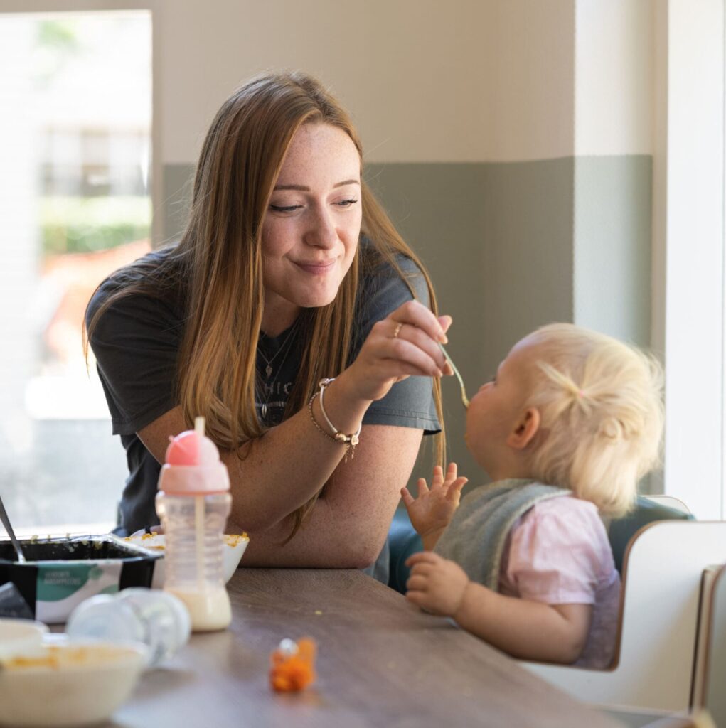 Pedagogisch professional begeleidt een baby tijdens een eetmoment bij Vlietkinderen in Leidschendam.