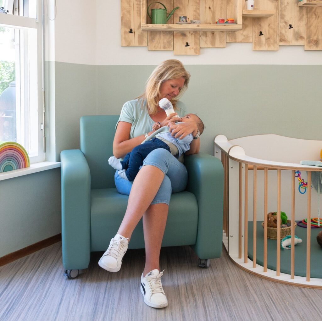 Pedagogisch medewerker geeft een fles aan een baby bij Vlietkinderen in Leidschenveen Den Haag.