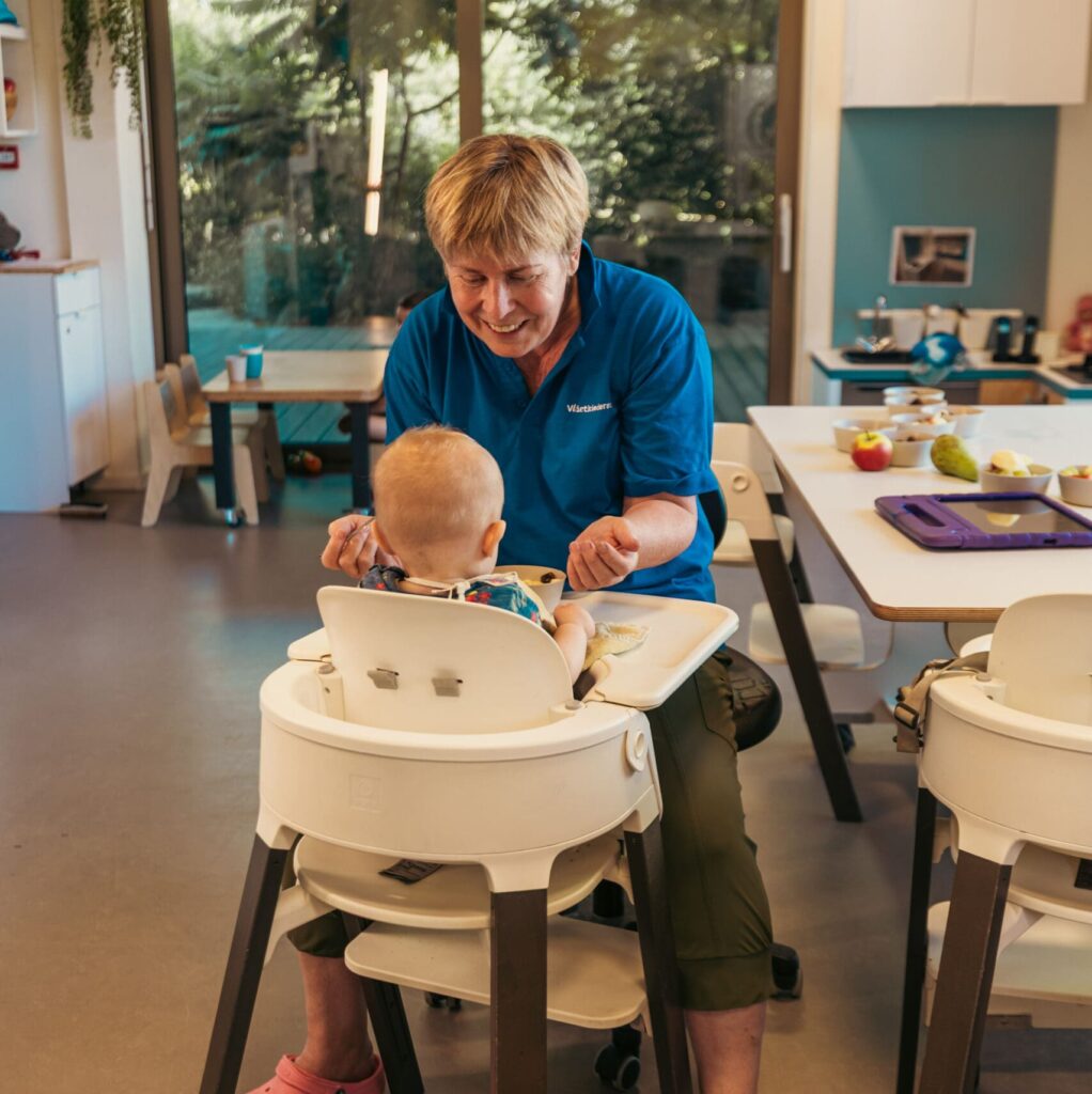Medewerker begeleidt een baby tijdens een eetmoment bij het kinderdagverblijf van Vlietkinderen in Voorburg.